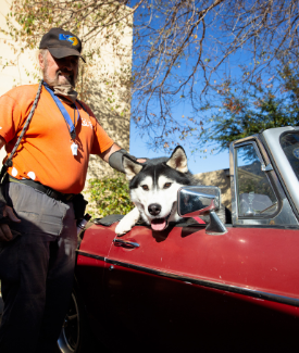 Dog sitting in red car with volunteer standing by